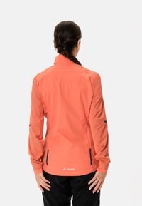 Korallfärgad vattentät jacka med hög krage, långa ärmar, sidofickor och svarta kontraster; slät textur, lätt design.