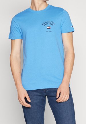 Jasnoniebieska bawełniana koszulka z okrągłym dekoltem, krótkimi rękawami i haftowanym logo "HILFIGER NEW YORK" powyżej "Est. 1985" na klatce piersiowej.