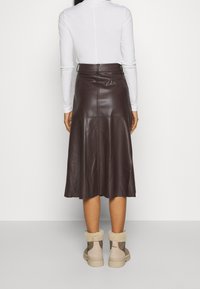 Bruine leren midi-rok met een uitlopende zoom, gecombineerd met beige en bruine enkellaarzen met een bontvoering, gedragen met een witte top met lange mouwen.