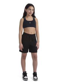 Melna sporta krūšturis ar baltu logotipu, melni šorti ar auklu viduklī un melni/balti sporta apavi. Gluda auduma un sportisks dizains.