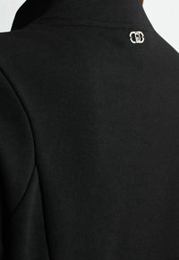 Felpa nera con tessuto liscio, collo alto e piccolo dettaglio logo metallico sul retro.