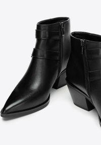 Schwarze Leder-Stiefeletten mit spitzen Zehen, Blockabsätzen, seitlichen Reißverschlüssen und dekorativen horizontalen Riemen über der Vorderseite.