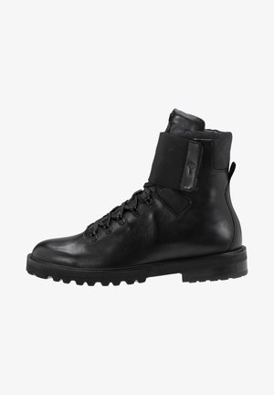 Bota de combate de cuero negro con suela de taco grueso, ganchos para cordones laterales, puño acolchado en el tobillo y cierre ancho de velcro.