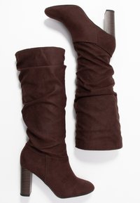 Bruna knähöga stövlar i mjuk mocka, med en avslappnad design, spetsig tå och kraftig ribbad klack.