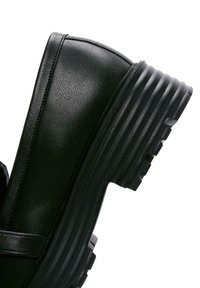 Zwarte enkelboot met een getextureerd leren bovenwerk, ronde neus en een dikke, geribbelde zool. Heeft een band over de wreef.