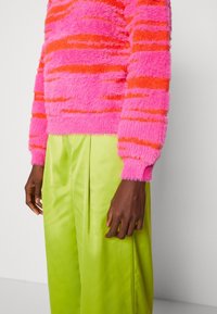 Pullover morbido a strisce rosa brillante e arancioni con maniche lunghe, abbinato a pantaloni larghi in satin verde lime lucido.