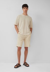 Beige textuurgebreide t-shirt en shortset met een ontspannen pasvorm. Gecombineerd met bruine sandalen met een platte zool en een eenvoudig bandontwerp.