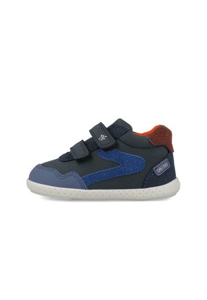 Zapatilla negra de niño con detalles en azul y marrón, dos tiras de velcro y una suela blanca con pequeños puntos.