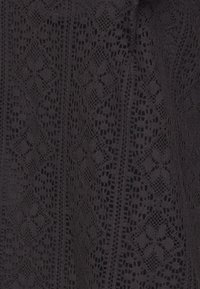 Tessuto in pizzo nero con intricati motivi a diamante e floreali che presentano un aspetto testurizzato, offrendo un design delicato e sofisticato.