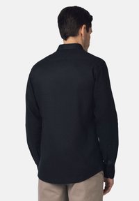 Czarna bluzka z długim rękawem, wykonana z teksturowanej tkaniny, z kołnierzykiem i zapinanymi mankietami. Prosty krój i zaokrąglony dół z tyłu.