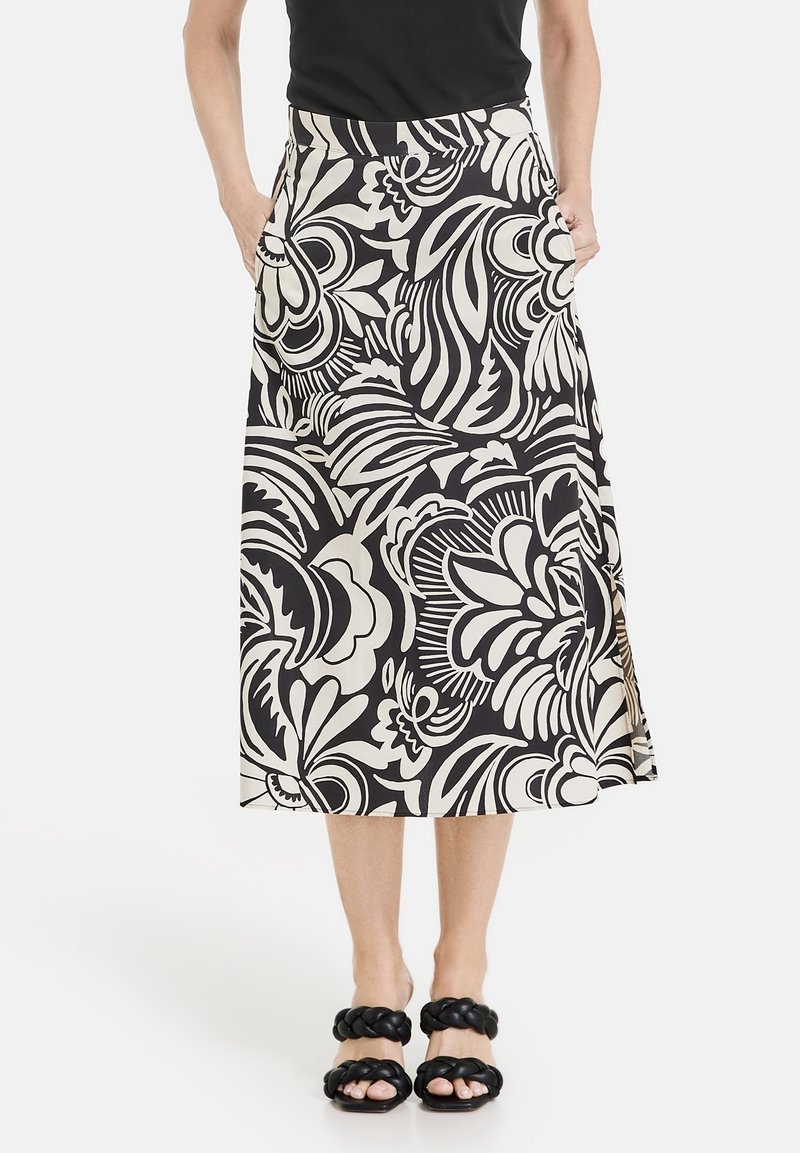 Une jupe midi à motifs floraux noir et blanc avec une taille ajustée, des poches latérales et une fente discrète. Associée à des sandales noires tressées.