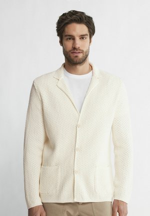 Gestrickte cremefarbene Strickjacke mit strukturiertem Muster, einreihigem Design, spitzen Revers, zwei Vorderaschen und Knopfverschlüssen.