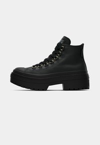 Zapatillas altas negras con suela gruesa, que presentan ojales dorados, cuero texturizado y un diseño de punta redonda.