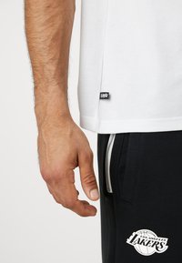 Witte katoen T-shirt met een zwart "EASY" label aan de zoom, gecombineerd met zwarte broek met een wit Los Angeles Lakers logo en een zilveren rits.