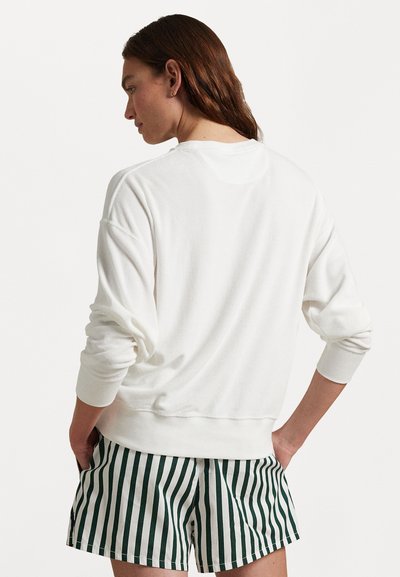 Hvit hettegenser med en avslappet passform, med ribbede mansjetter og nederkant. Kombinert med grønne og hvite stripete shorts, som viser en uformell stil.