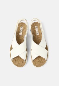 White cork-soled sandals feature cross-strap design with a smooth finish. The brand name "CAMPER" is printed on the insoles.