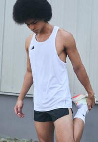 Hvid sports tanktop med sort logo, parret med sorte shorts. Stoffet ser let og åndbart ud, velegnet til fitnessaktiviteter.