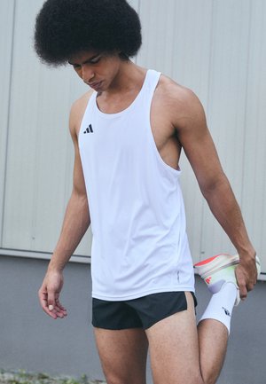 Débardeur de sport blanc avec logo noir, associé à un short noir. Le tissu semble léger et respirant, adapté aux activités de fitness.