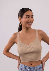 Beige geripptes Crop-Top mit V-Ausschnitt und verstellbaren Trägern. Kombiniert mit hellgewaschenen Denim-Shorts.