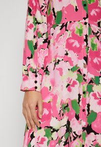 Floral dress in pink, green, and black featuring a button-up front and long sleeves. Fabric has a smooth texture with vivid abstract patterns.