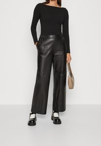 Musta leveälahkeiset nahkahousut, joissa on sileä pinta, sivutaskut ja rento istuvuus, yhdistettynä istuvaan mustaan pitkähihaiseen puseroon.