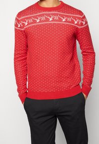 Maglione lavorato a maglia rosso con un motivo di renna sul petto, dettagli in bianco e un design testurizzato a pois su tutta la superficie.