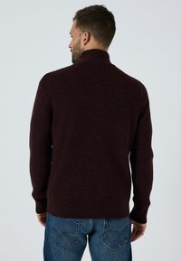 Burgunderfarbener Strickpullover mit hohem Kragen, Strukturstoff und gerippten Bündchen, kombiniert mit blauen Jeans. Ansicht von hinten.