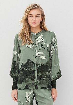 Grön skjorta med knappar och svart bergs- samt blommönster. Mjuk tyg, lös passform och långa ärmar med texturerade manschetter.