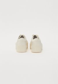Baskets plateforme en matériau synthétique crème clair, design arrondi, semelle en caoutchouc texturée et talon avec des détails de surpiqûre subtils.