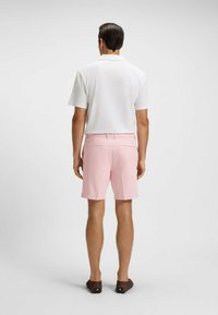 White short-sleeve polo shirt paired with light pink shorts. The shorts have back pockets and a tailored fit, complemented by brown footwear.