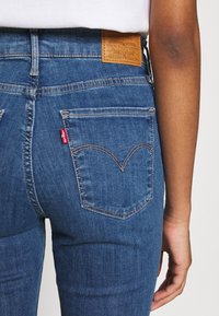 Mörkblå denimjeans med hög midja, utrustade med en läderetikett på baksidan och en distinkt röd flik på vänster bakficka.