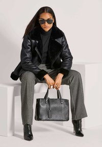 Zwarte leren jas met nepbontkraag, zwarte coltrui, broek met pied-de-poule patroon, zwarte handtas en zwarte laarzen met hoge hak.