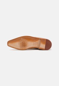 Sole di scarpa in pelle color marrone chiaro con forma appuntita. Presenta dettagli intricati in rilievo e una texture liscia, che mettono in mostra il brand e le informazioni sulla taglia.
