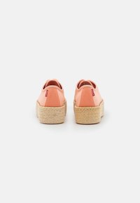 Espadrilles en toile rose avec une tige en textile, semelle enveloppée de jute et bout arrondi. À l'arrière, on trouve une petite étiquette rouge.