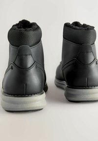 Botas de cuero negro hasta el tobillo con cuello de malla texturizada, interior acolchado y suela de goma gris. Detalles cosidos en la parte trasera y en los lados.