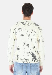 Maglione girocollo in crema con motivo a macchie nere. Texture lavorata a maglia, polsini e orlo a coste, vestibilità comoda, tessuto di peso medio.