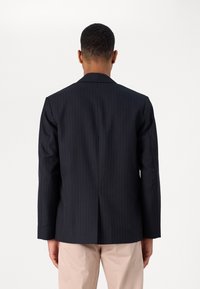 Maßgeschneiderter Marineblazer mit Nadelstreifenmuster, einfachem Rückenschlitz und Revers mit Kerbverschluss. Der Stoff hat eine glatte Textur.