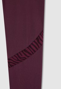 Leggings bordeaux con un design curvo e una pannello in rete a strisce zebrate nere e rosa lungo un lato. Tessuto liscio ed elasticizzato.