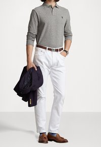 Graues langärmeliges Polohemd mit Kragen, weiße gerade Hosen, braune Lederloafers und ein dunkelblauer Blazer, der im linken Arm gehalten wird.