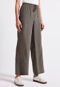 Lätta, olivgröna vida byxor med elastisk midja, snörningsdetalj och framfickor. Materialet verkar vara texturerat och andningsbart.