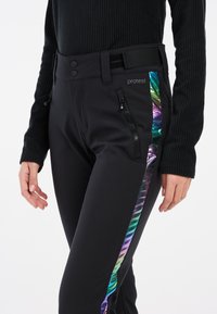 Zwarte sportbroek met een glanzende iriserende streep langs de zijkant, met ritszakken en een aansluitend ontwerp voor flexibiliteit.