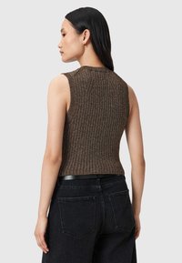 Brązowy prążkowany bezrękawnik z teksturowanej tkaniny, o dopasowanym kroju i zaokrąglonym dekolcie, w połączeniu z czarnymi jeansami o wysokim stanie.