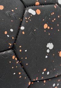 Svart texturerad yta med orange, vit och grå stänkmönster. Hexagonal form med präglade pilar på panelerna.