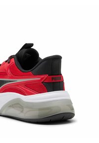 Scarpa da ginnastica rossa con accenti neri, tomaia in mesh, collo imbottito e logo sul tallone. Presenta una suola intermedia bianca e una suola esterna traslucida.