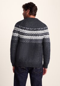 Dark gray knitted sweater with a white and light gray zigzag pattern at the shoulders, ribbed cuffs, and hem, featuring a relaxed fit.