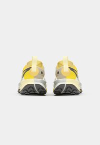 Des chaussures avec un dessus principalement jaune, des accents gris, un col rembourré et une semelle extérieure en caoutchouc noir texturé avec un motif de semelle.