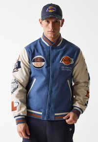 Blue wool blend varsity jacket with beige leather sleeves, featuring layered Los Angeles Lakers logos and embroidered details.