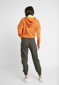 Orange hoodie kombinerad med olivgröna cargobyxor med elastiska ärmslut och sidofickor. Vita sneakers fulländar outfiten.