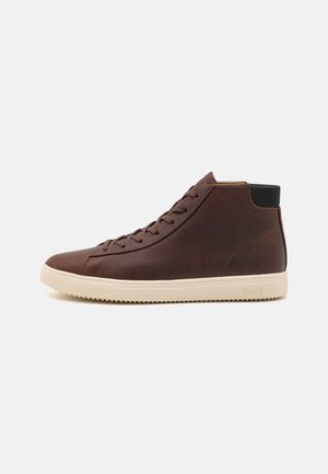 Brown leather high-top sneaker with tonal laces, a textured finish, and a contrasting cream rubber sole. Features a black heel tab.
