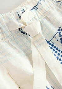 Close-up van lichte stof met blauw geruit en bloemmotieven, met een elastische tailleband en een geknoopt stoffen strik.